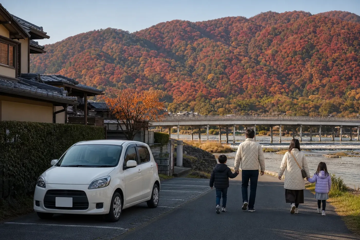 11月の朝、赤や橙に色づいた山と川、遠くに長い橋が見える嵐山で、住宅の駐車スペースに白い車を停めた家族4人が川沿いを歩いている写真風のイメージ（AI生成）