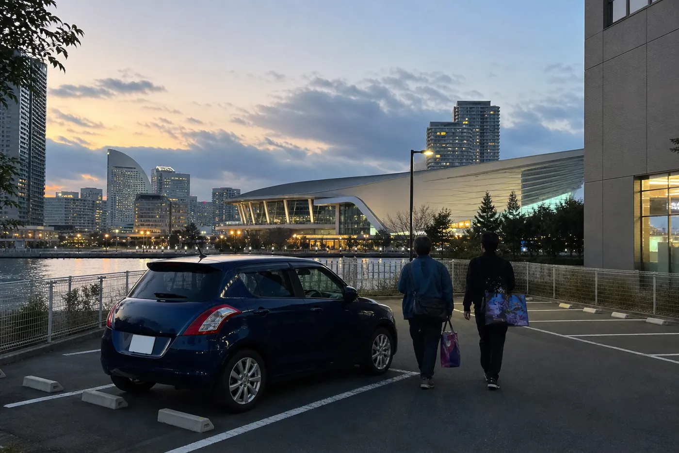 夕暮れの横浜の湾岸で、オフィスビル裏の駐車場に紺色の車が停まり、ライブグッズの袋を持った2人が海沿いの大きなアリーナに向かって歩いている写真風のイメージ(AI生成)