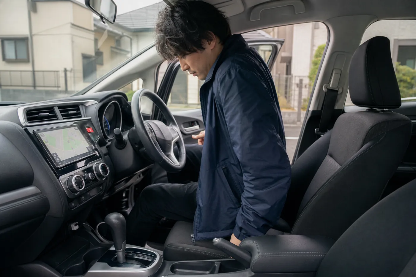 朝の自宅の駐車場で、上着のポケットにスマホを入れたまま運転席に乗り込む人と、すでに地図が映っている純正ナビのイメージ(AI生成)