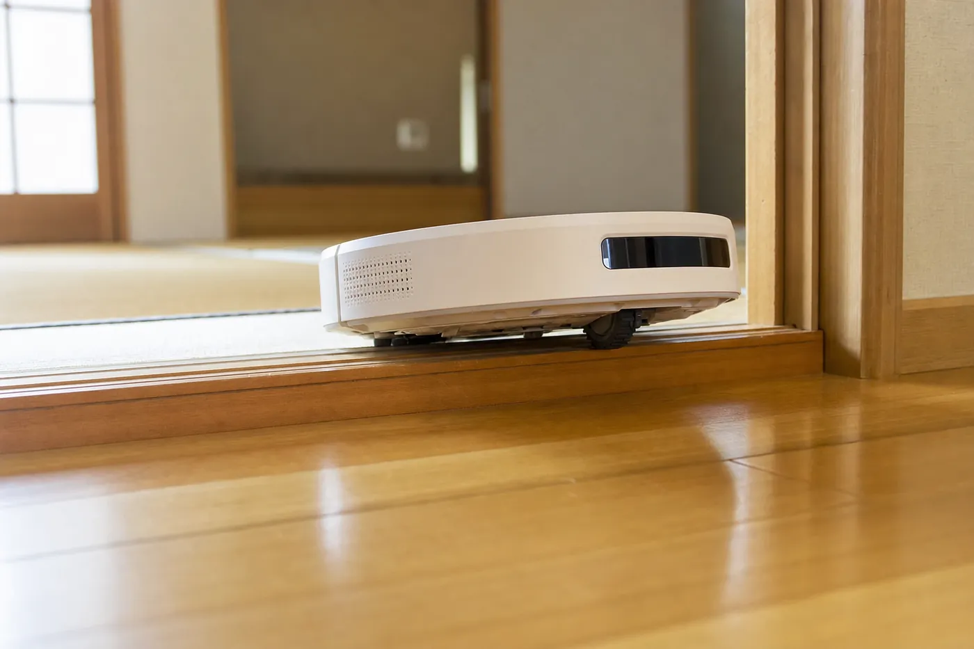 廊下と和室のあいだの木の敷居を、ロボット掃除機が乗り越えようとしている写真風のイメージ