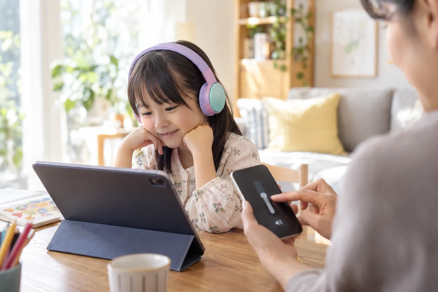 ヘッドホンをつけた子どもと、スマートフォンで音量を調整する親のイメージ