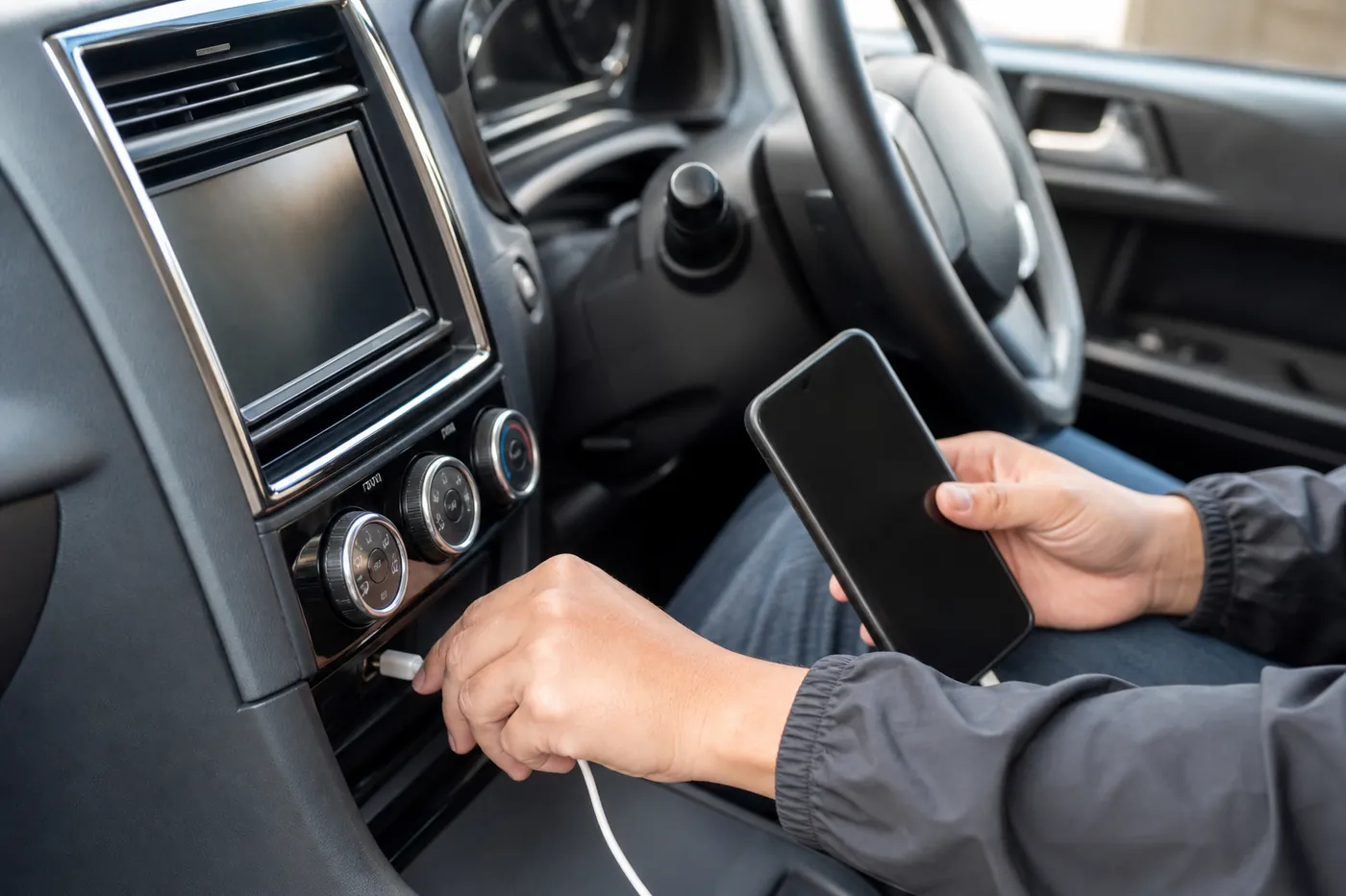 止めた車の中で、スマホを片手に持ち、純正ナビの下の USB にケーブルを挿しているイメージ(AI生成)